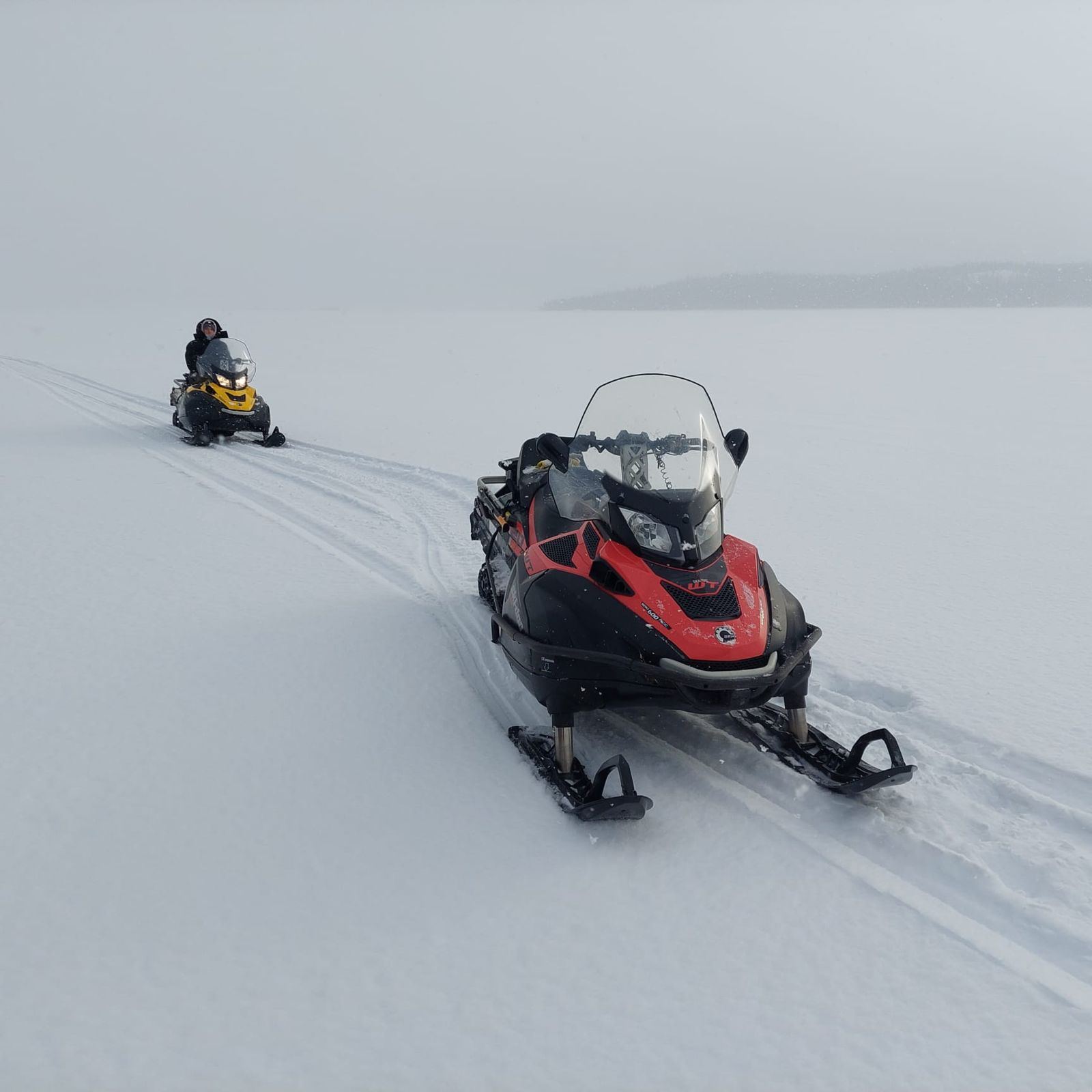 Deux motoneiges en file sur un lac gelé sous la neige